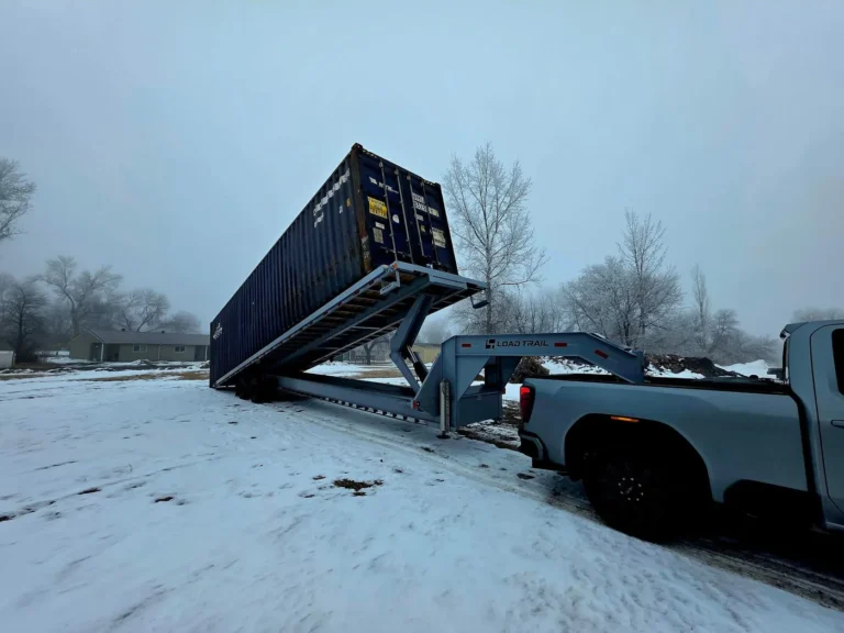 A 40ft shipping container being unloaded from a tilt bed trailer in the snow