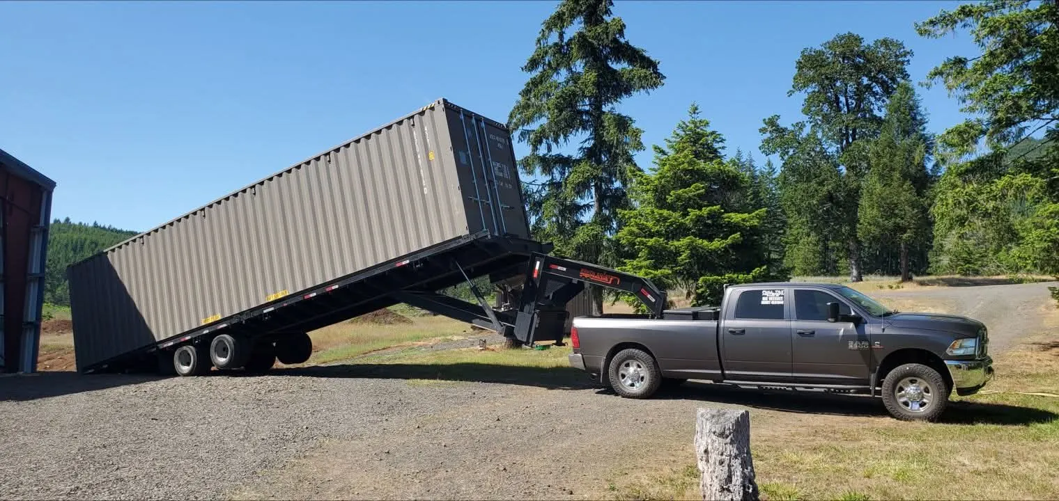 Tilt-bed truck tilting a shipping container onto the ground during delivery