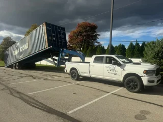 A white pickup truck with a tilt bed trailer tilting a shipping container